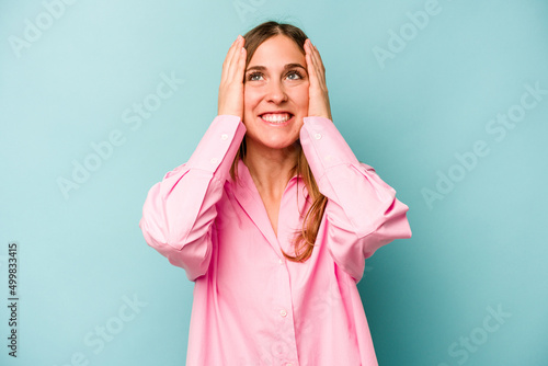 Young caucasian woman isolated on blue background laughs joyfully keeping hands on head. Happiness concept.