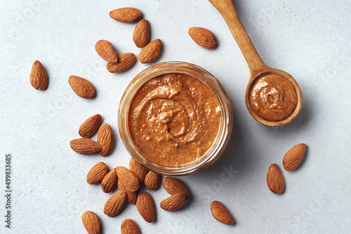 Glass jar and spoon of almond butter on light gray background