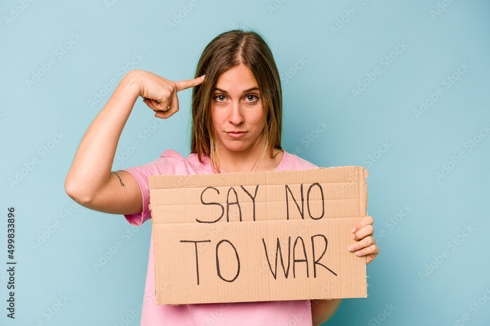 Young caucasian woman holding no war placard isolated on blue background Young caucasian woman holding no war placard isolated on blue background