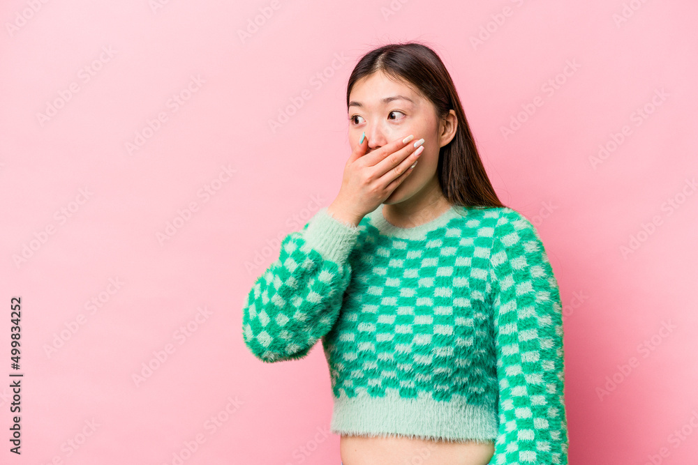 Young Chinese woman isolated on pink background thoughtful looking to a copy space covering mouth with hand. Young Chinese woman isolated on pink background thoughtful looking to a copy space covering mouth with hand.