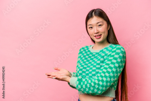 Young Chinese woman isolated on pink background holding a copy space on a palm. © Asier
