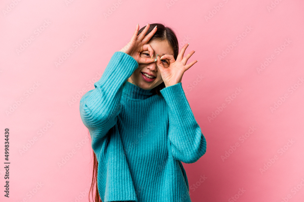 Young Chinese woman isolated on pink background showing okay sign over eyes Young Chinese woman isolated on pink background showing okay sign over eyes