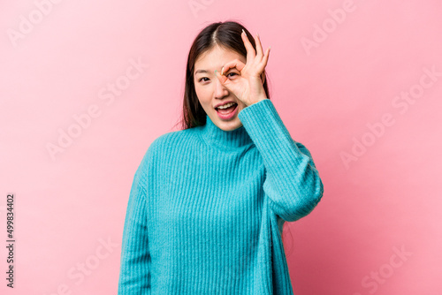 Young Chinese woman isolated on pink background excited keeping ok gesture on eye. © Asier