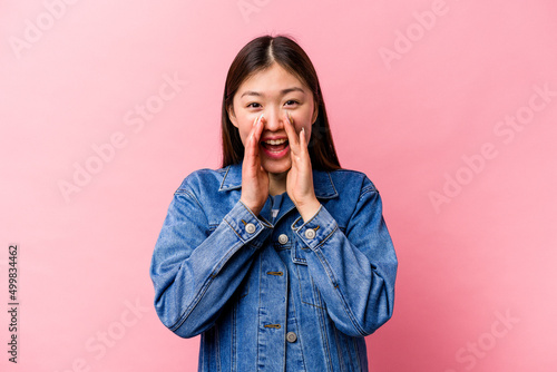 Young Chinese woman isolated on pink background saying a gossip, pointing to side reporting something.