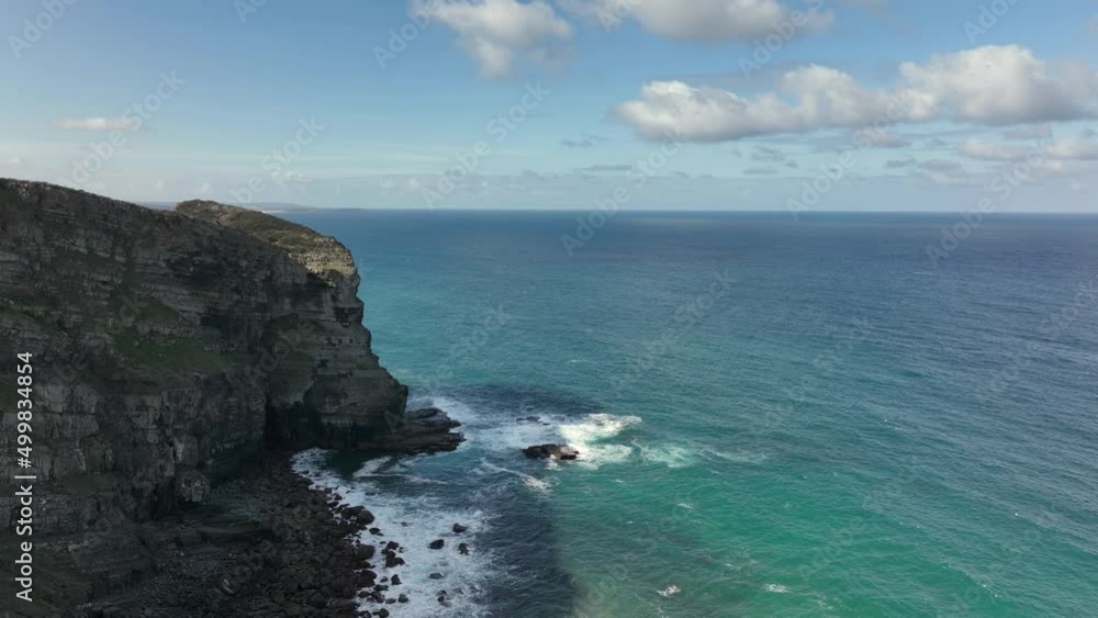 Aerial reveal shot flying along rugged cliffs by a beautiful turquoise ocean on a sunny day