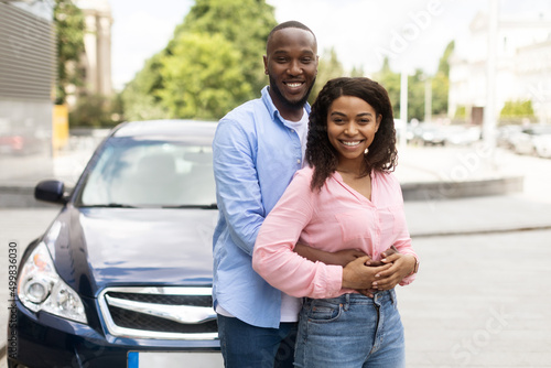 Happy black couple standing near car and hugging