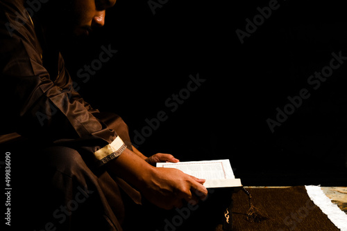 Selective focus picture of a men reading Holy Quran on copyspace dark background. Always Quran concept. photo