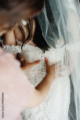 Morning preparation A bridesmaid helping the bride to button up her white wedding dress Bridesmaid's hands fastening wedding dress buttons Wedding day concept Bridal dress with naked back Close up 