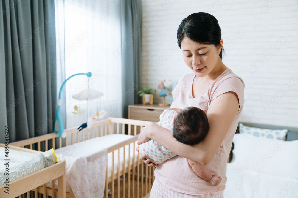 portrait of asian mother trying to rock her newborn baby to sleep. pretty korean mom who loves her daughter dearly is humming softly at naptime. portrait of asian mother trying to rock her newborn baby to sleep. pretty korean mom who loves her daughter dearly is humming softly at naptime.