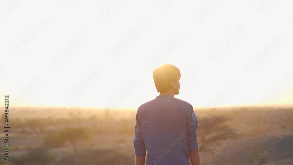 Portrait of an Indian man walking in front of sun during the sunset. Lonely man walks during the sunset. Loneliness concept. Man walks alone to think for his future. Portrait of an Indian man walking in front of sun during the sunset. Lonely man walks during the sunset. Loneliness concept. Man walks alone to think for his future.