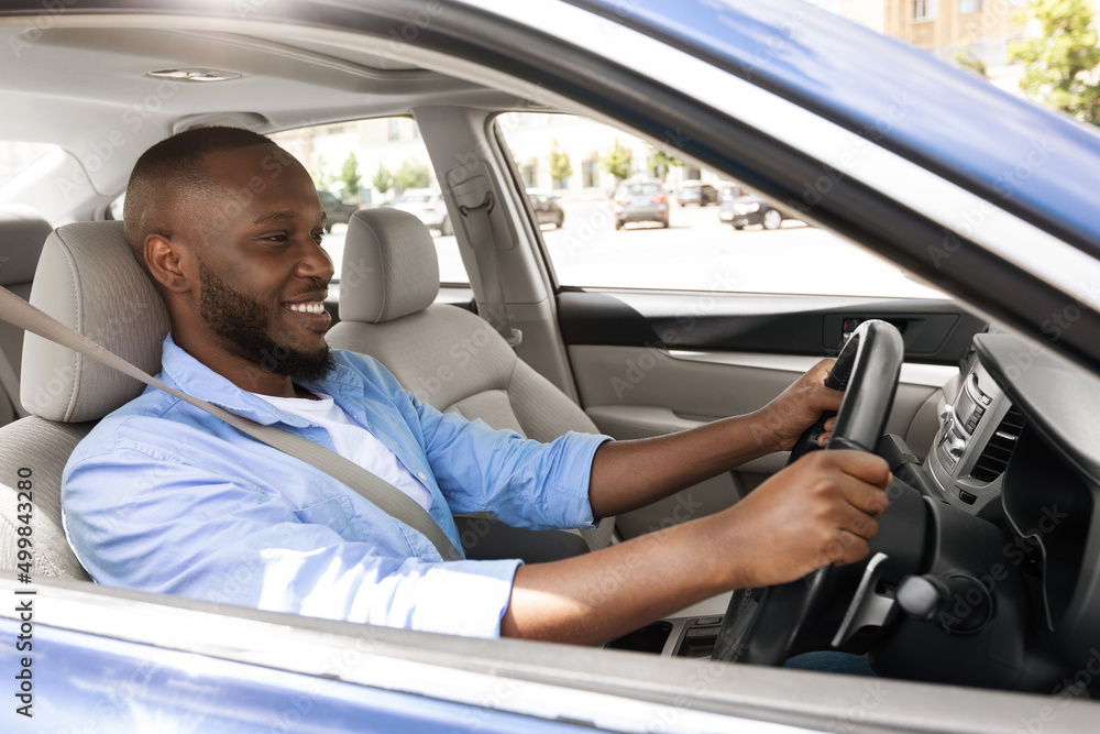 Smiling black guy driving new car in city