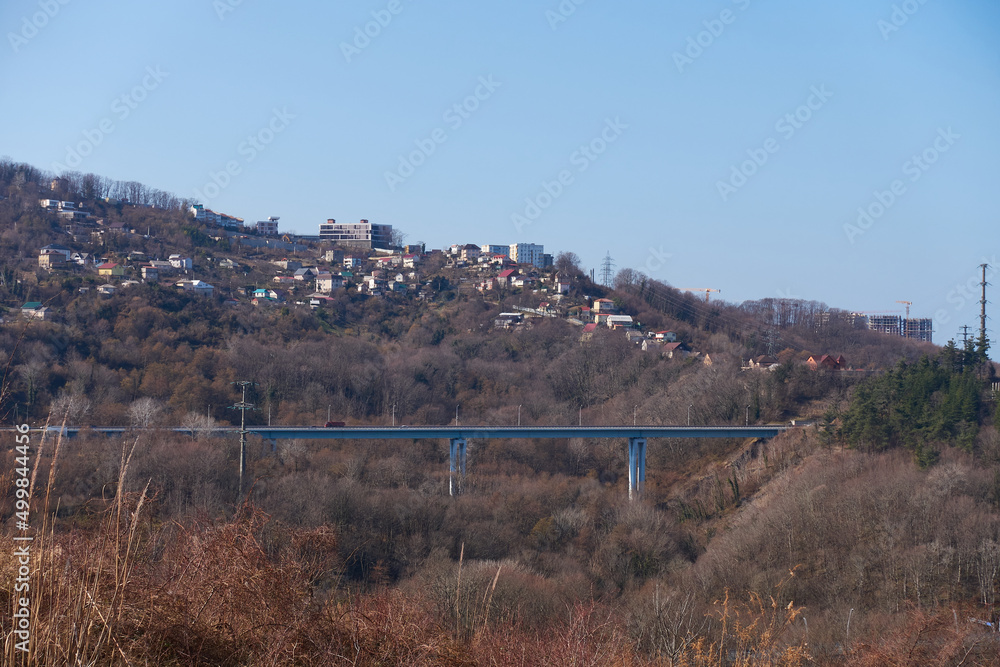 Automobile bridge on high concrete pillars connecting the gorge. Built and unfinished houses are located on the mountainside. Winter in the resort town.