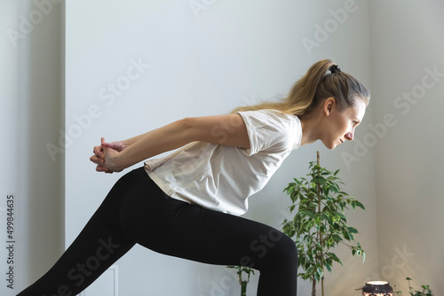 young slim woman is stretching her arms, opening chest, holding arms behind, leaning forward to her leg, profile portrait of practice at home