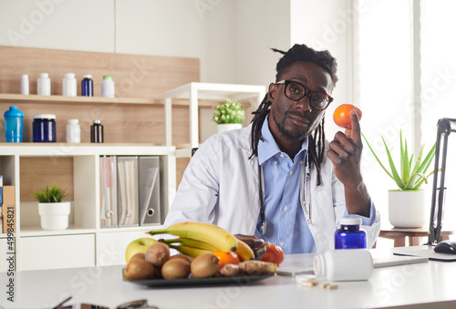Afroamerican nutritionist looking at camera and showing healthy fruits in the consultation.