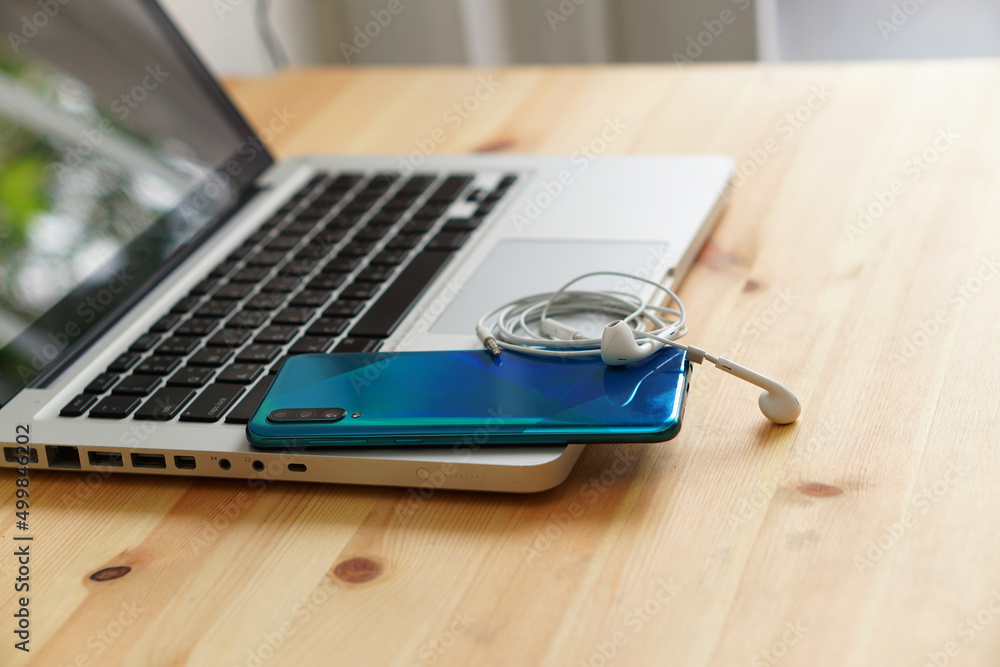 Smartphone and earphones on the laptop computer, electronic gadgets for daily use on wooden background. Smartphone and earphones on the laptop computer, electronic gadgets for daily use on wooden background.
