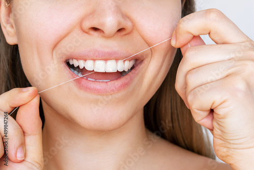 A cropped shot of a young caucasian blonde woman flossing her teeth after meal. Close-up. Dental health care  oral hygiene  morning and evening routine. Dentistry concept