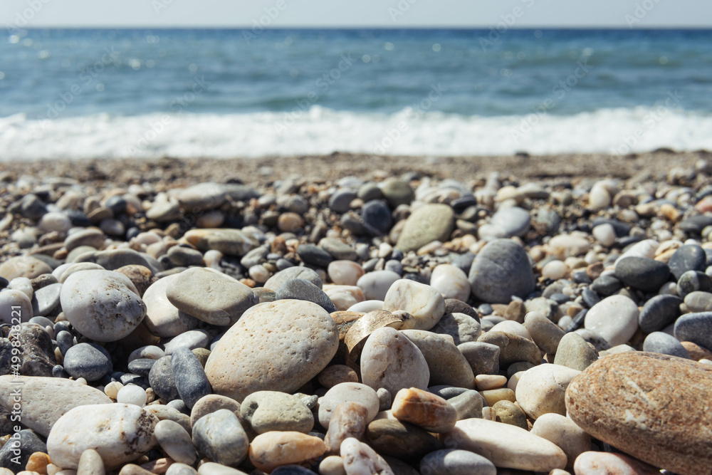 a beach with dark and light pebbles, blue sea, there is a background a beach with dark and light pebbles, blue sea, there is a background