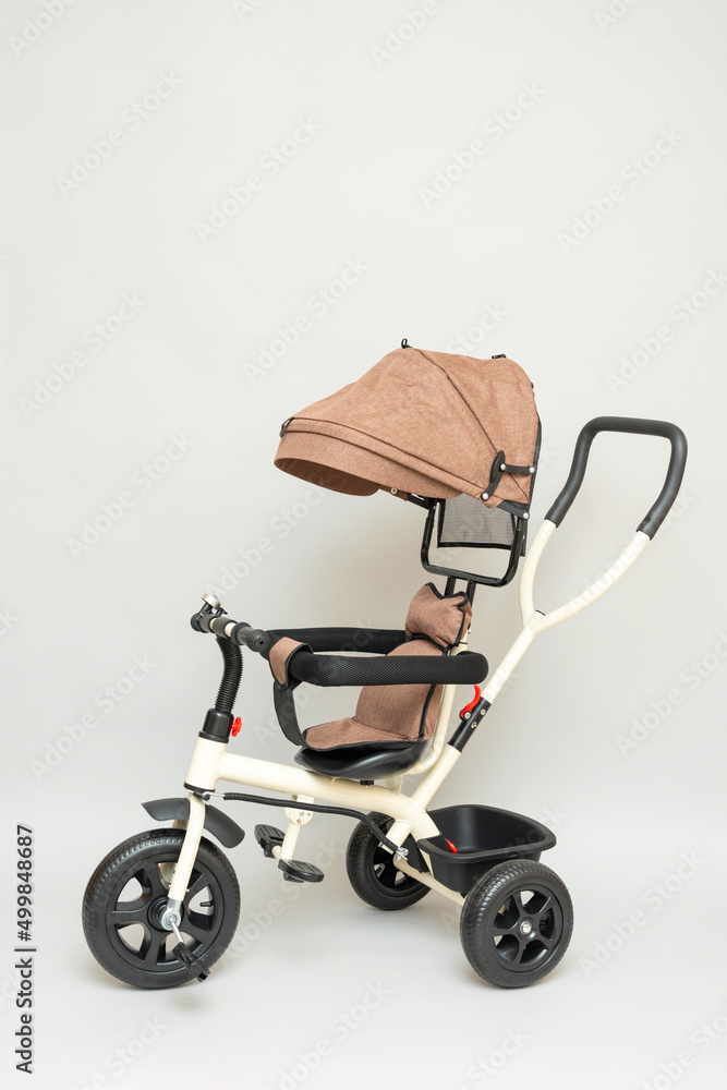 Beige modern children's three-wheeled stroller with a handle for control and pedals on a gray background Beige modern children's three-wheeled stroller with a handle for control and pedals on a gray background