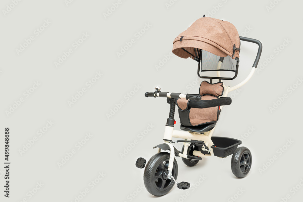 Beige children's tricycle with handle on gray background, copy space Beige children's tricycle with handle on gray background, copy space