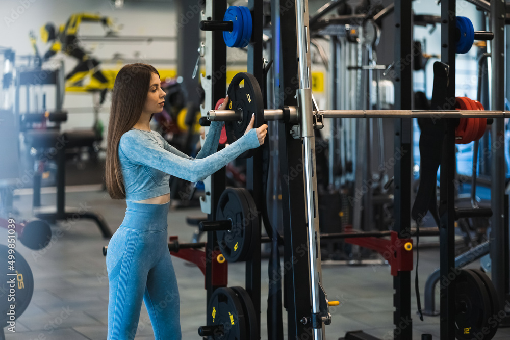 Athletic woman puts the disc on the smith machine. Girl exercising in the gym Athletic woman puts the disc on the smith machine. Girl exercising in the gym