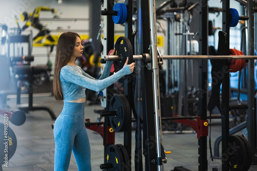 Fotografia Athletic woman puts the disc on the smith machine