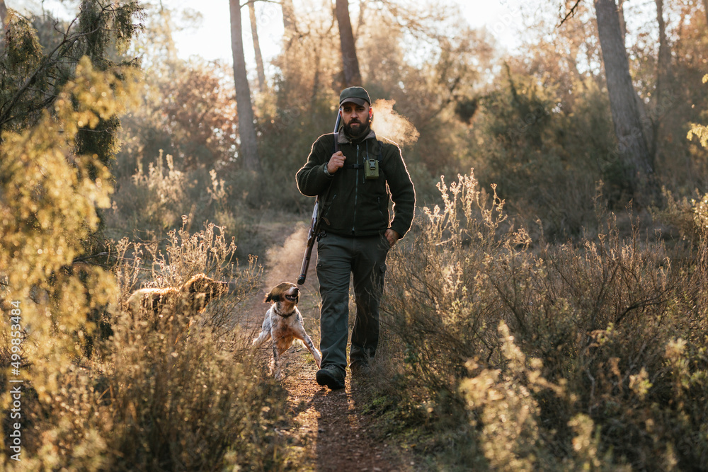 Man walking straight ahead carrying his gun with his dogs running around