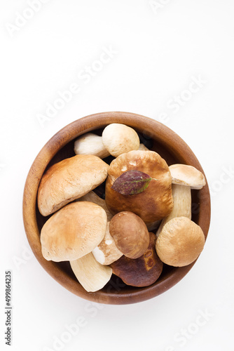 Bunch of fresh forest porcini mushrooms in a round wooden bowl on a white background close up, soft focus, top view, copy space 