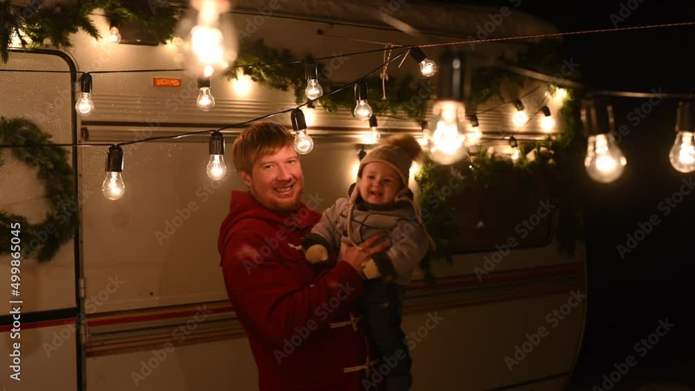 Caucasian red-haired man with a boy in his arms at the mobile home. Father and son celebrate Christmas on a trip. Caucasian red-haired man with a boy in his arms at the mobile home. Father and son celebrate Christmas on a trip.