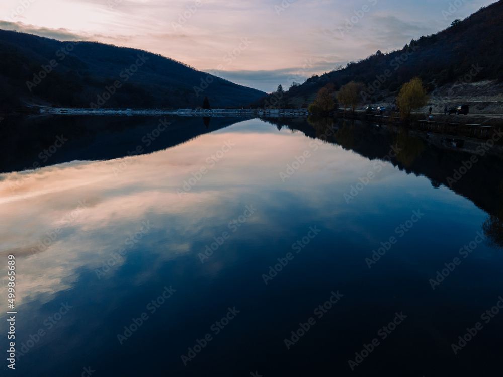 A beautiful mirror lake reflects the sky at sunset. Autumn forest in the mountains. Beautiful sky. People are resting on the shore of a mountain lake.