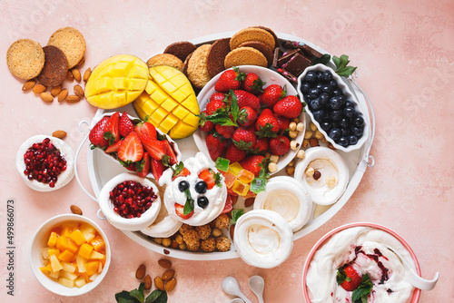 Pavlova grazing platter with pavlova nests, fresh fruits, ginger cookies, toppings, chocolate and whipped cream. Top view, blank space