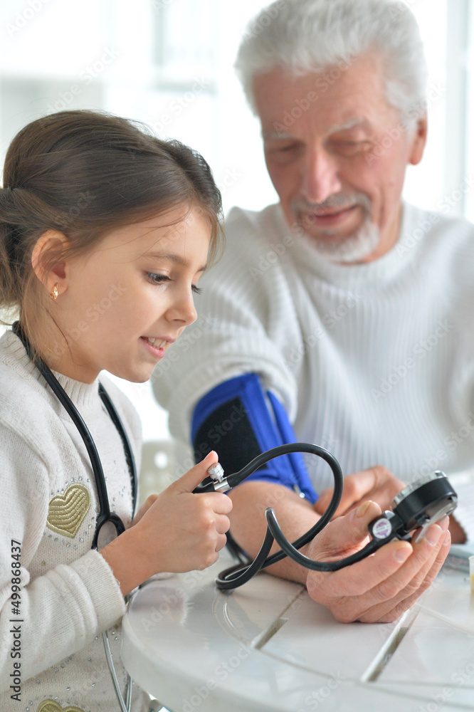 Obraz premium Portrait of granddaughter measuring blood pressure to her grandfather in room