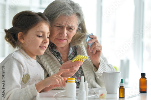 Cute girl giving medicine to sick senior woman