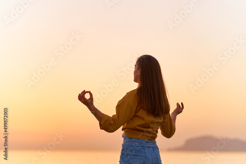 Fototapeta Back view of blissful serene satisfied one calm woman standing alone on the beach by the sea