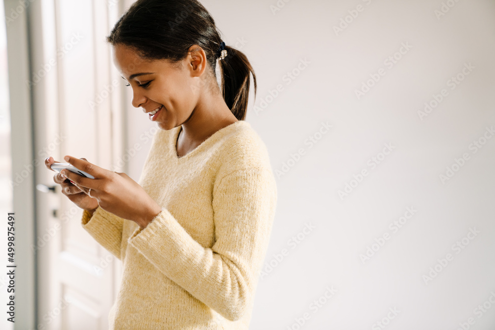 Black girl using mobile phone while standing at home Black girl using mobile phone while standing at home
