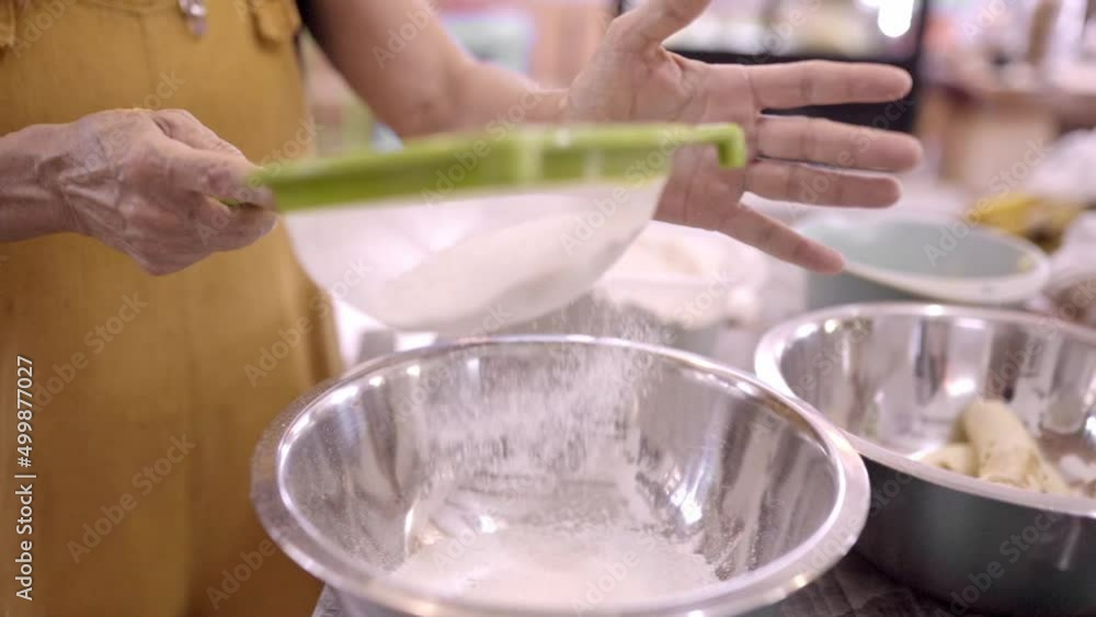 Mature woman sifting flour in metal bowl in kitchen Mature woman sifting flour in metal bowl in kitchen