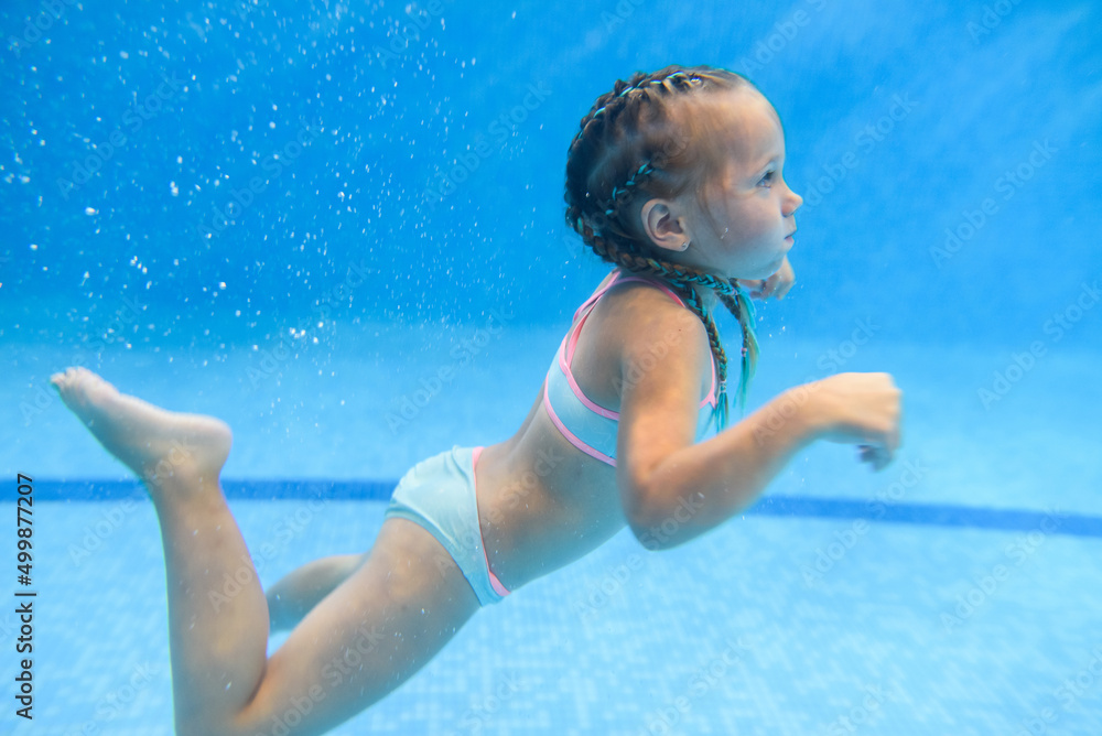 Little child girl swimming underwater in the paddling pool. Diving. Learning infant child to swim. Enjoy swimming and bubbles.