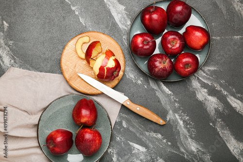Fresh ripe whole and peeled red apples with cutting board and knife on stone table