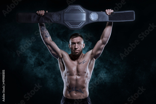 Vászonkép Kickboxer victoriously raises the belt won in the tournament against the backdrop of smoke