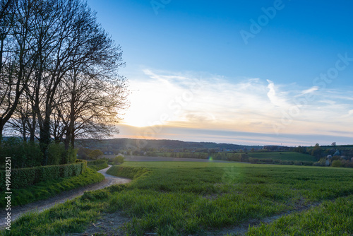 A spring landscape with rolling hills in the south of Limburg during a spectacular sunset with a dirt road which seems to lead to the sun