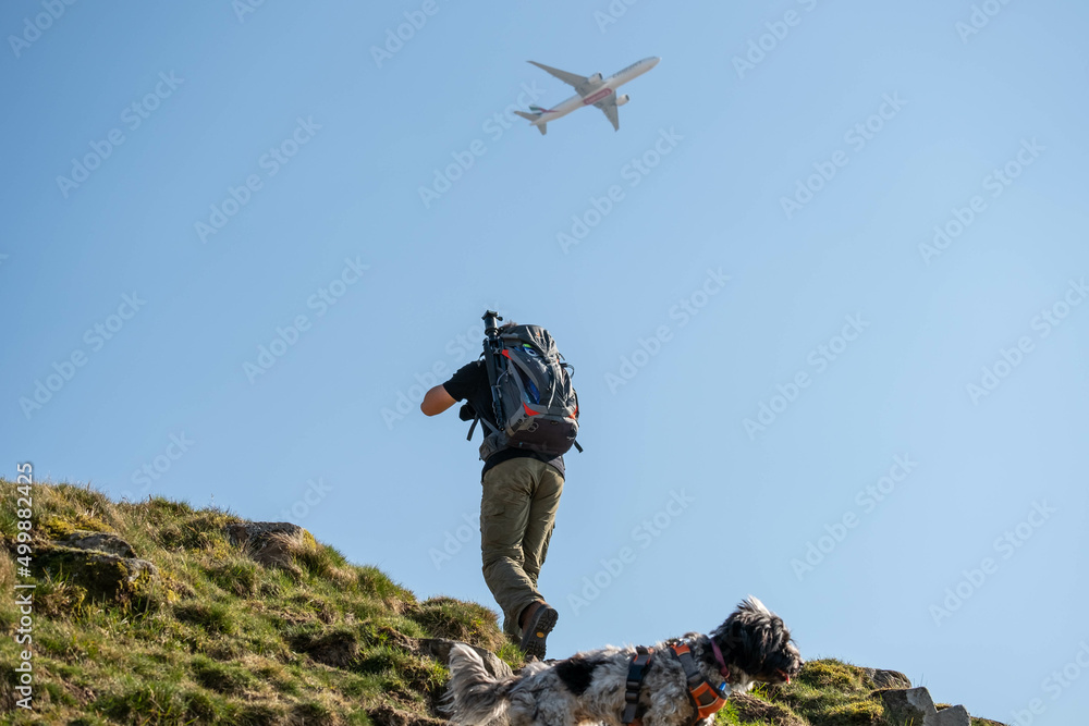 Fototapeta premium Man with camera equipment hiking while plane flies overhead - location scouting