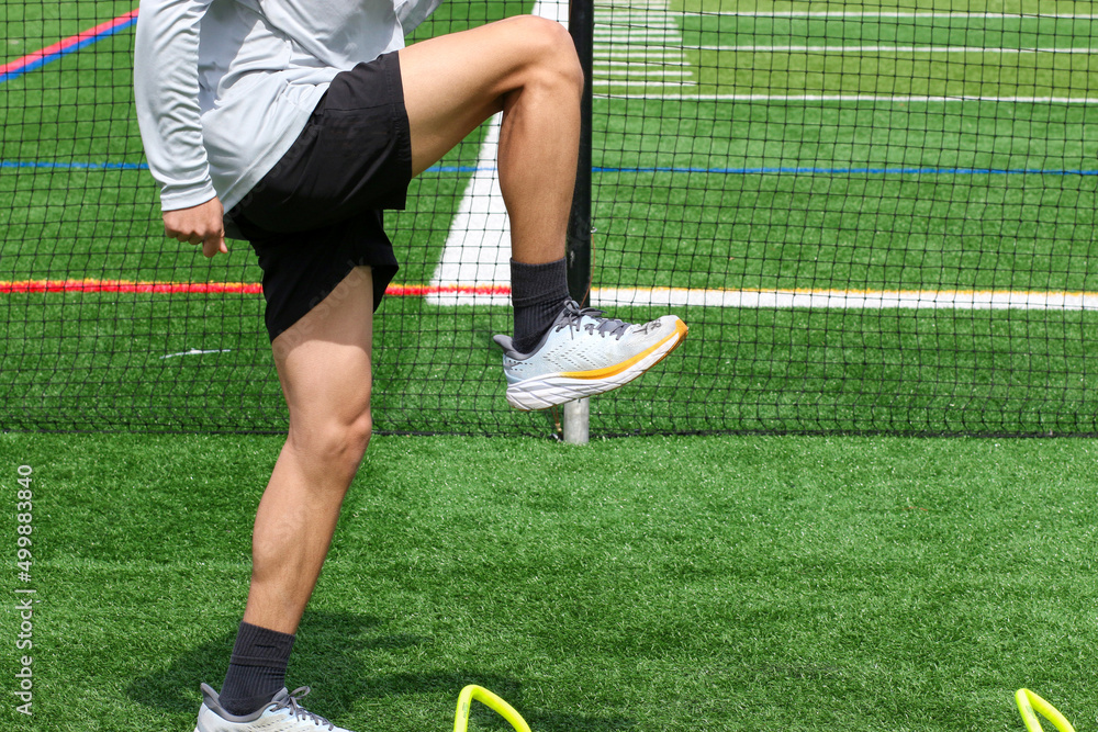 Athlete standing over small yellow hurdles on a green turf field Stock