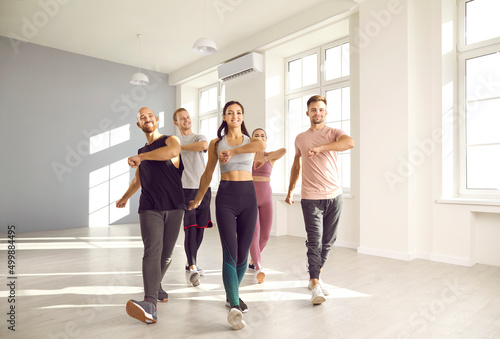 Sports, healthy lifestyle and fitness. Group of happy young people doing sports exercises together while training in fitness studio. Smiling men and women in sportswear are taking steps together.
