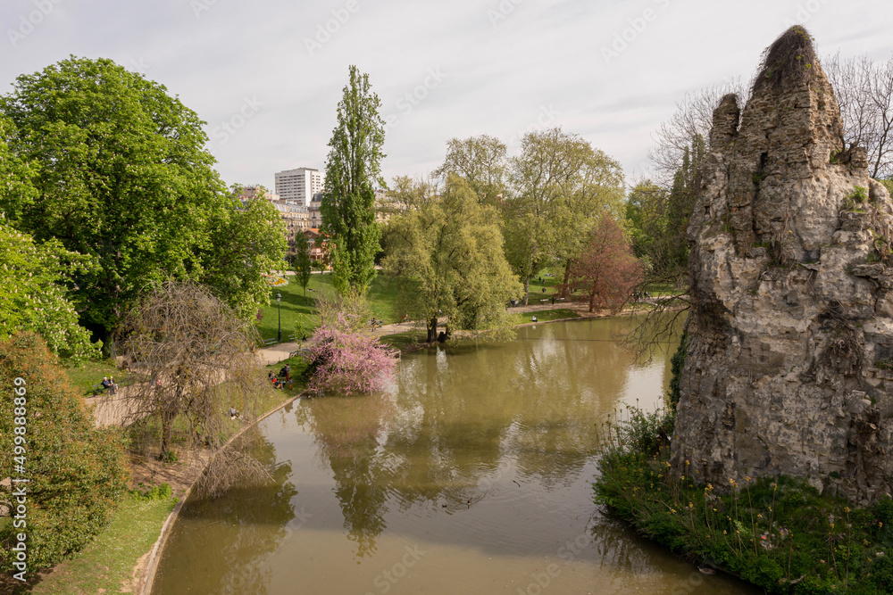 Paris, France - 04 10 2022: Park des Buttes Chaumont. View of the Sugarloaf shaped rock in the belvedere Island near Footbridge