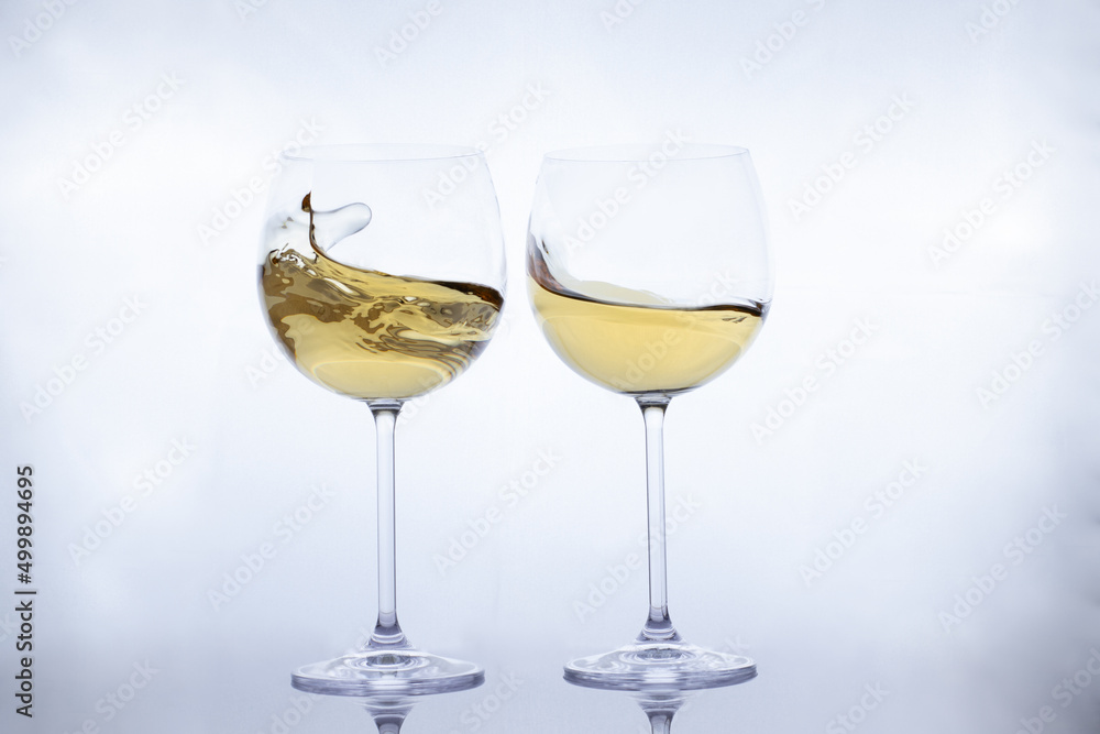 two white wine glasses with moving liquid on a greyish-white background