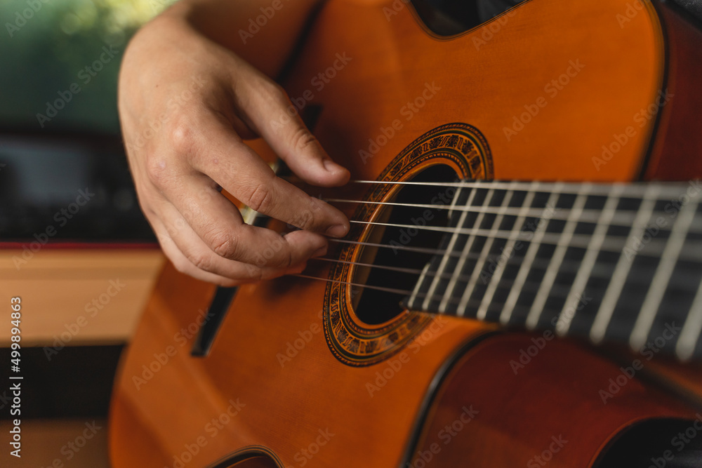 Fototapeta premium A young guy is playing a classical guitar in his room during the day