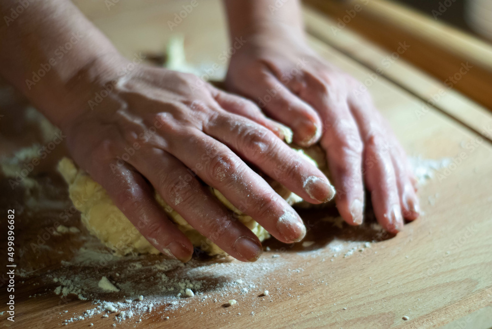 Baker's hands working the flour dough on a wooden board