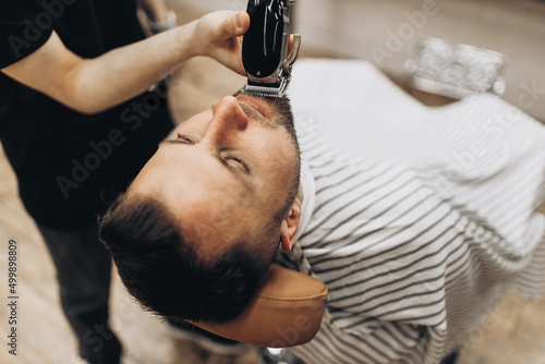 Barber cuts his beard to man in armchair