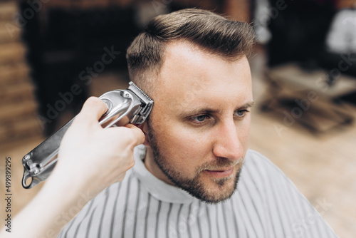 Barber shearing beard to man in barbershop framing hairline. electric razor, vintage tinted brown