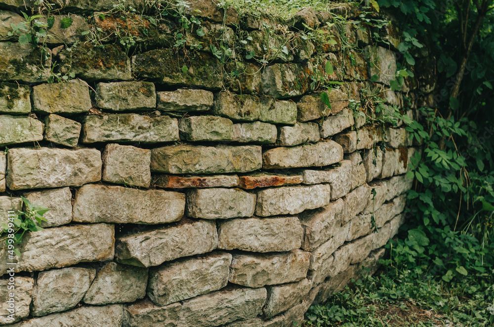 Paved wall with a rough, clear texture and deep lines between large stones. Laying an old fence. Destroyed stone fence.