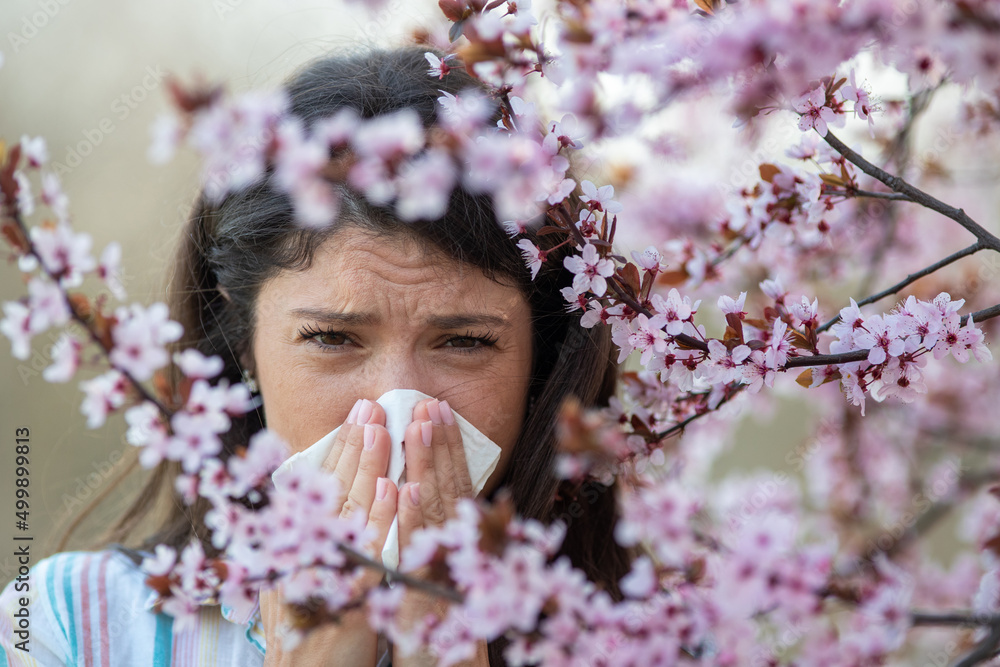 Obraz premium Girl wiping nose in front of blooming tree in spring